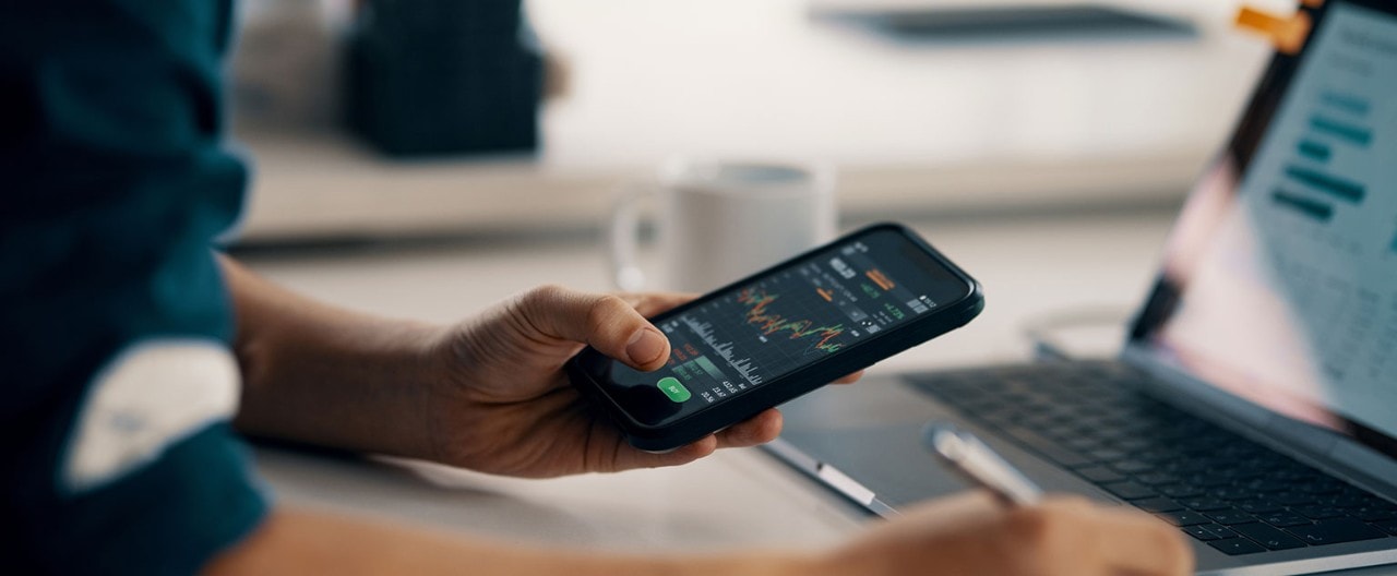 Man reviewing financial data on smartphone and laptop