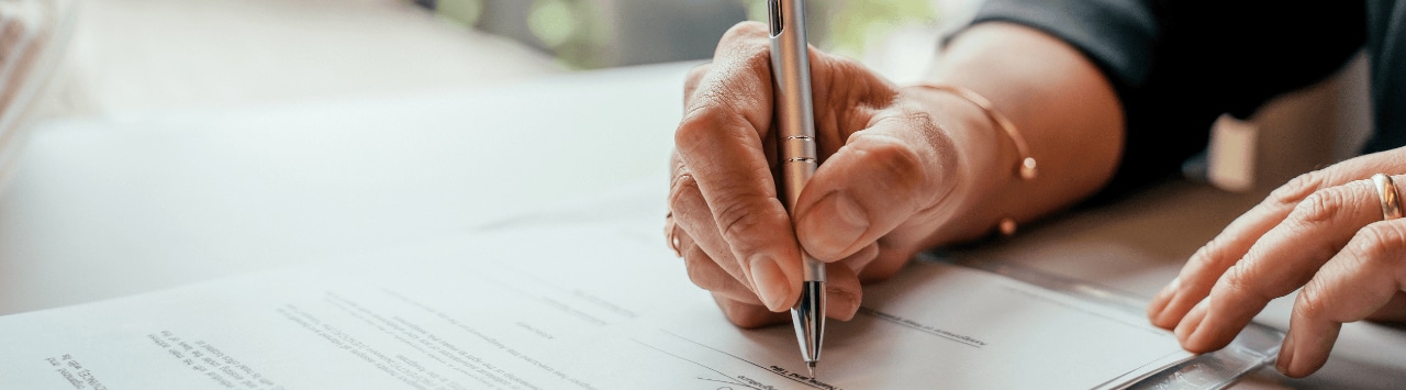 Person signing financial documents with a pen during a professional meeting
