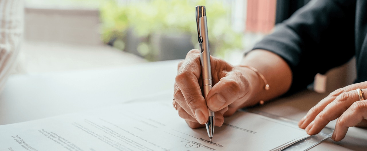 Person signing financial documents with a pen during a professional meeting