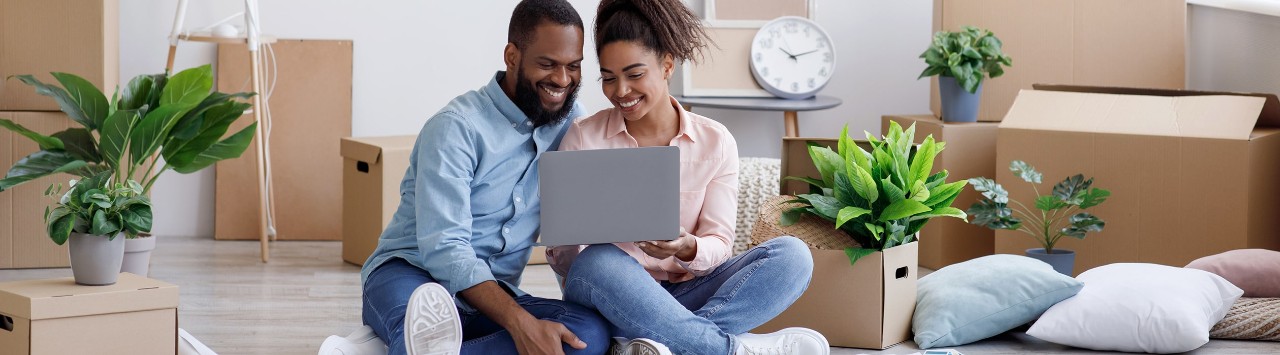 Young African-American couple sitting on floor using laptop surrounded by moving boxes