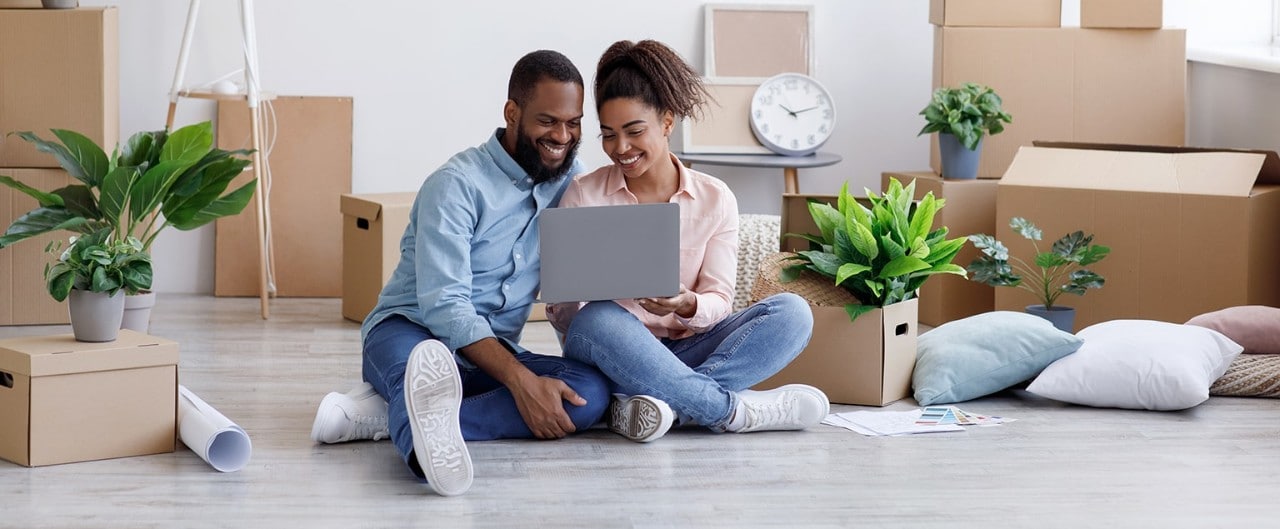 Young African-American couple sitting on floor using laptop surrounded by moving boxes