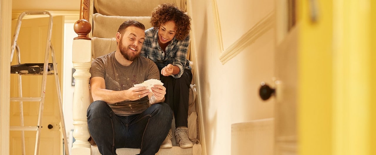 Mixed race couple renovating home sitting on steps looking at paint swatches