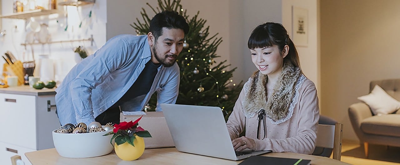 Asian couple at kitchen table looking at desktop during holidays