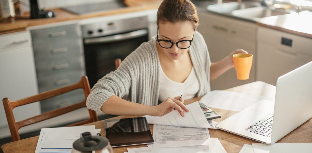 Woman sitting at kitchen table drinking coffee and paying bills