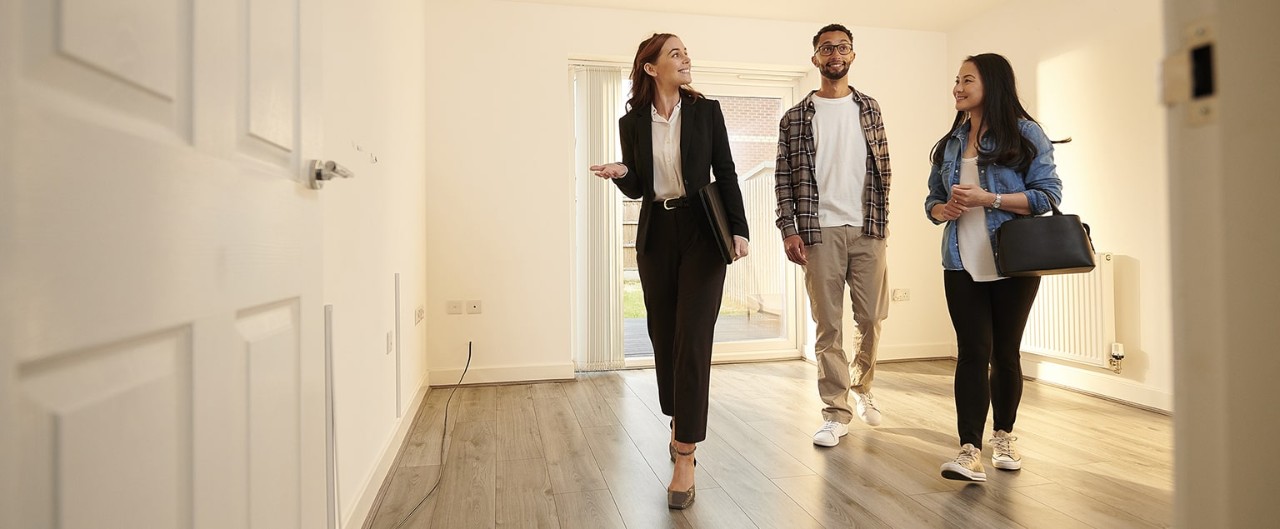 Happy young couple walking through empty home with realtor