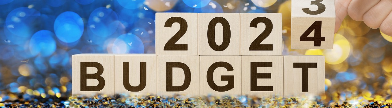 Woman flipping wooden cube from 2023 budget to 2024 budget on confetti background