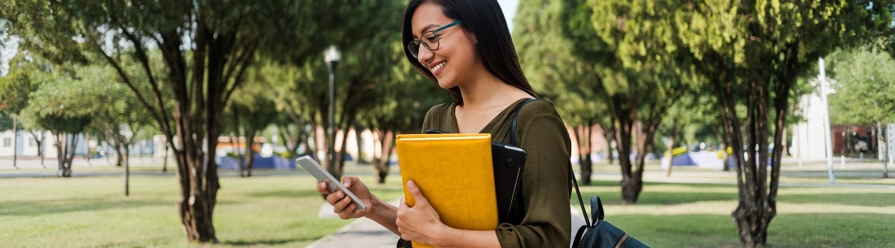 Female Hispanic college student wearing backpack, holding leather portfolio and a smartphone
