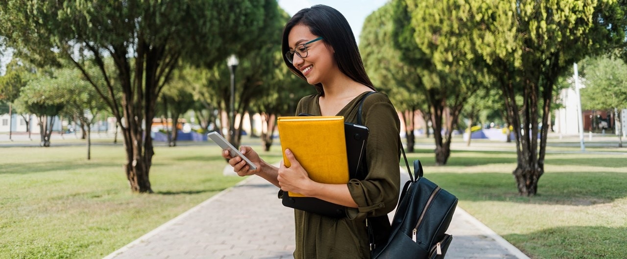 Female Hispanic college student wearing backpack, holding leather portfolio and a smartphone