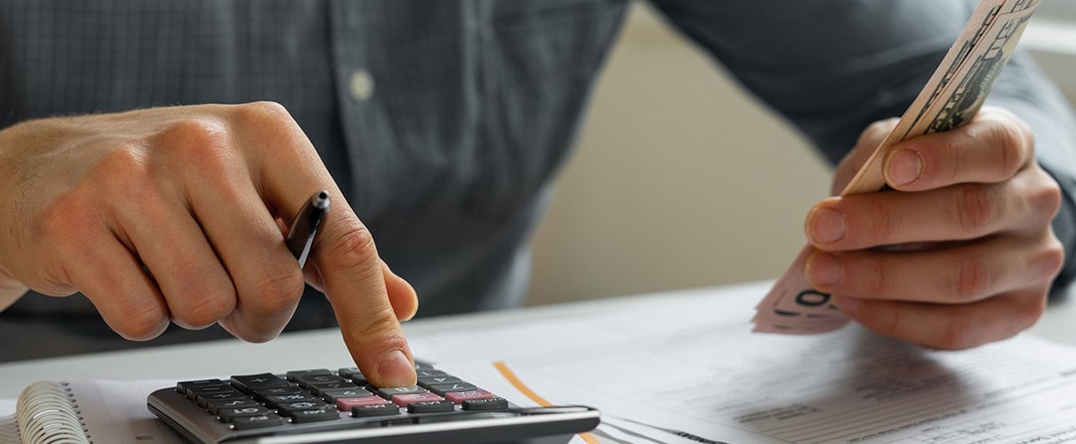 Man has cash in one hand and is using a calculator with the other hand