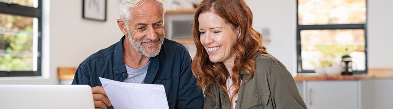 Couple sitting at table reviewing papers and using laptop