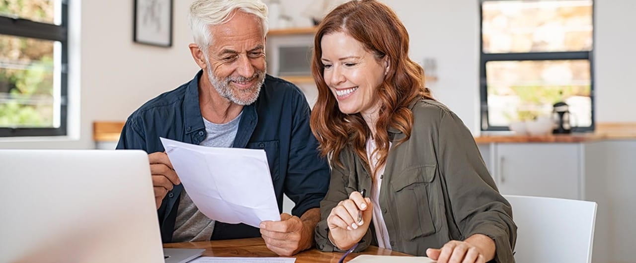 Couple sitting at table reviewing papers and using laptop