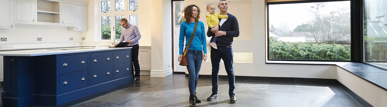 Diverse couple holding young child looking at new home with realtor standing by kitchen cabinets