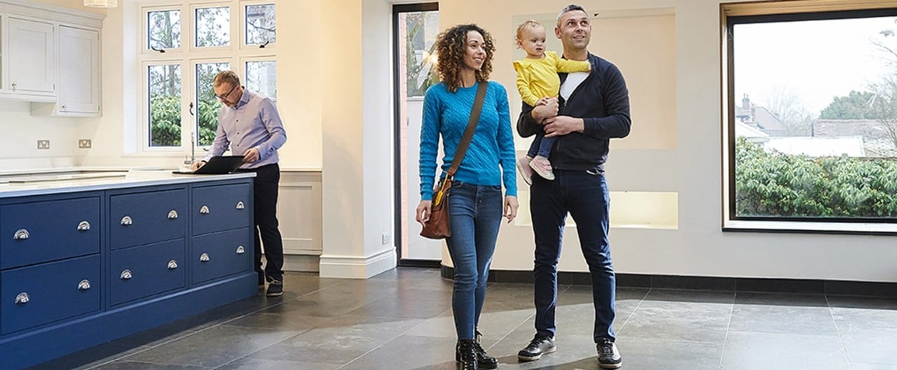 Diverse couple holding young child looking at new home with realtor standing by kitchen cabinets