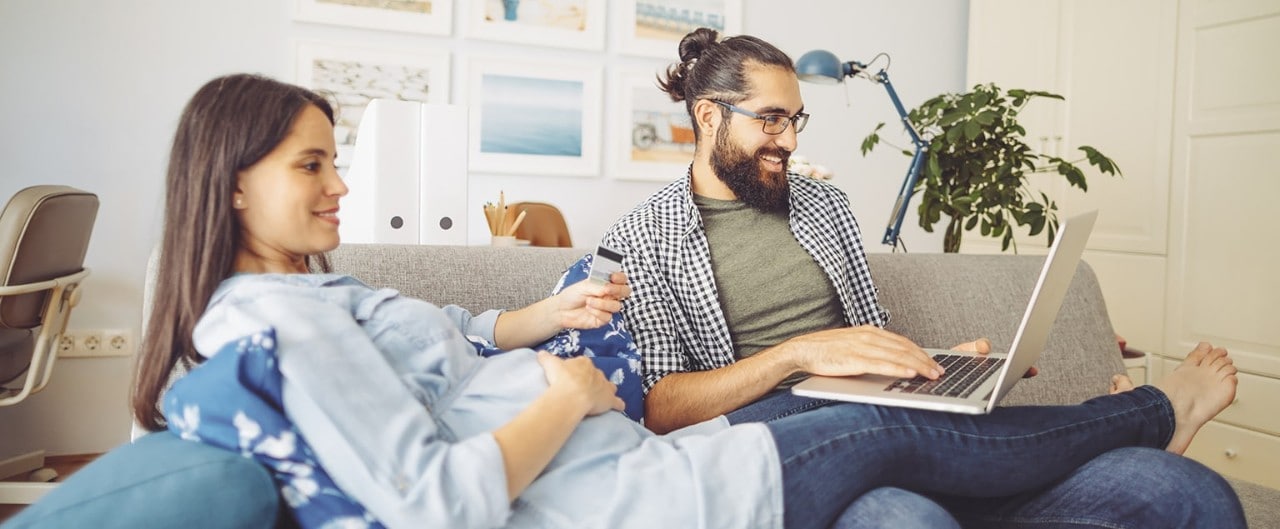 Man using laptop on couch with pregnant wife