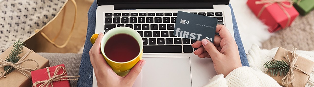 Woman holding First Financial Rewards card and a cup of coffee looking at laptop surrounded by holiday gifts