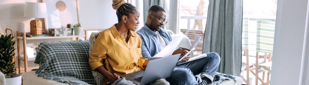 African-American couple sitting on couch reviewing financial documents