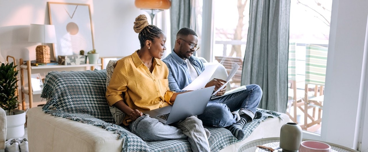 African-American couple sitting on couch reviewing financial documents