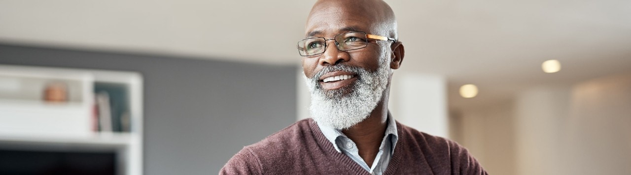 Smiling senior African-American man sitting alone in his living room and thinking how to use strategic asset allocation