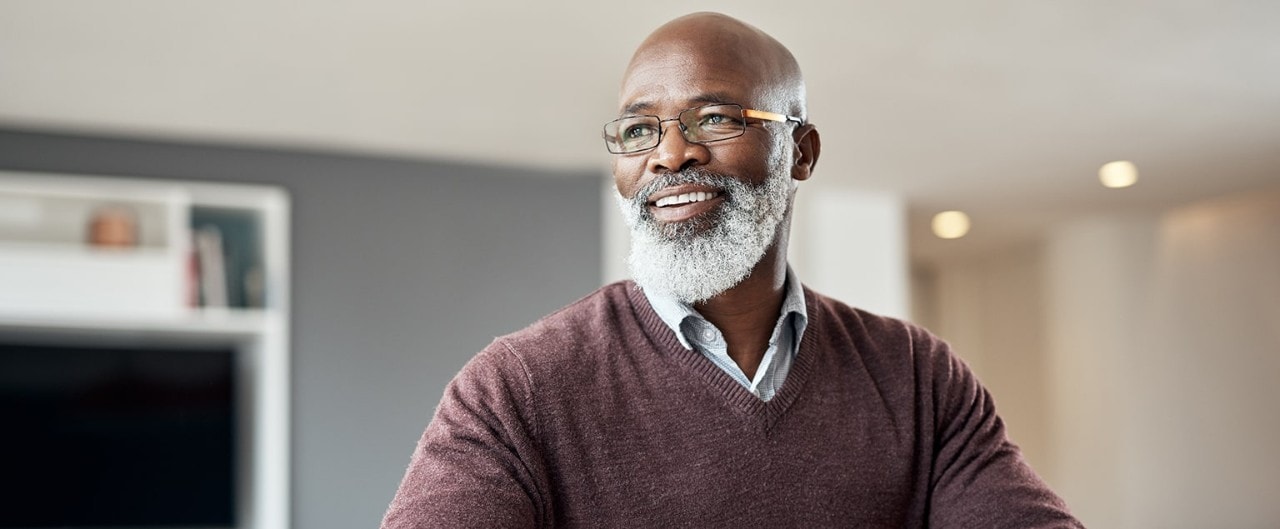 Smiling senior African-American man sitting alone in his living room and thinking how to use strategic asset allocation
