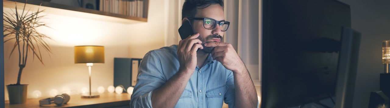 Concerned man talking on smartphone and looking at computer monitor