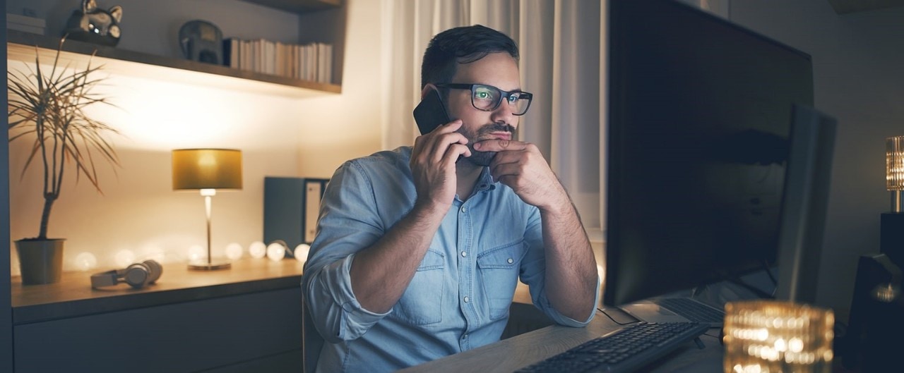 Concerned man talking on smartphone and looking at computer monitor