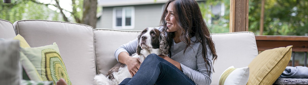 Woman snuggling with dog on outdoor patio sofa
