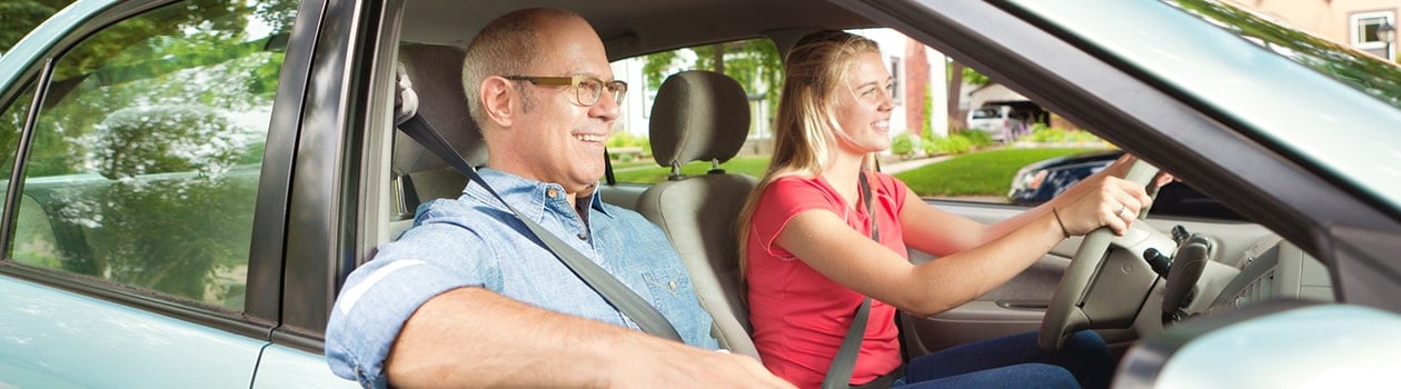 Happy father supervising teen daughter driving in her new car