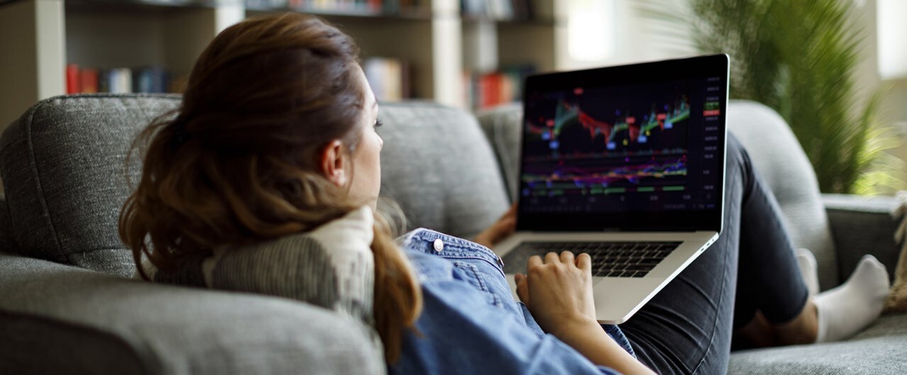 Woman on couch reviewing financial data on laptop