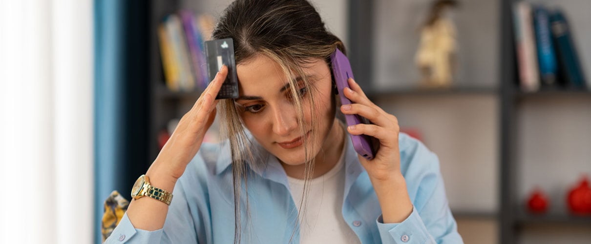 Concerned young woman talking on smartphone and holding credit card