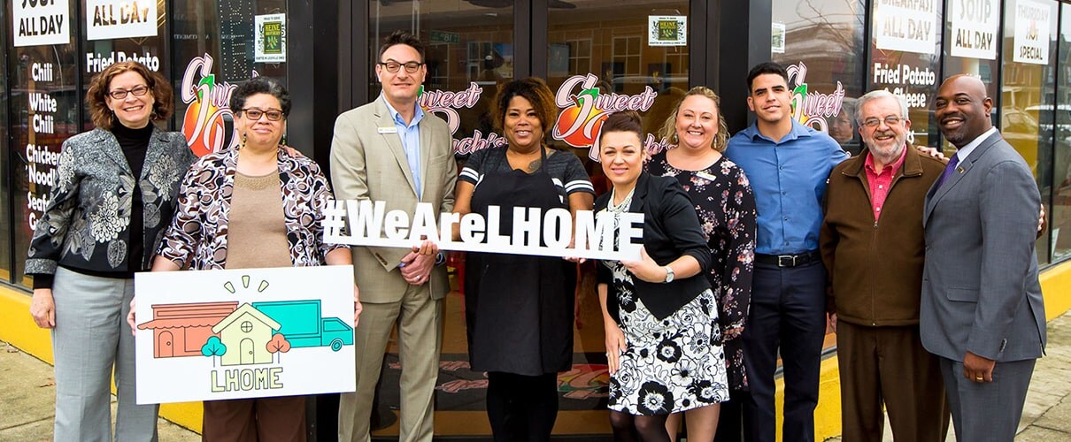 Diverse group of people holding a #WeAreLHOME sign and an LHOME sign