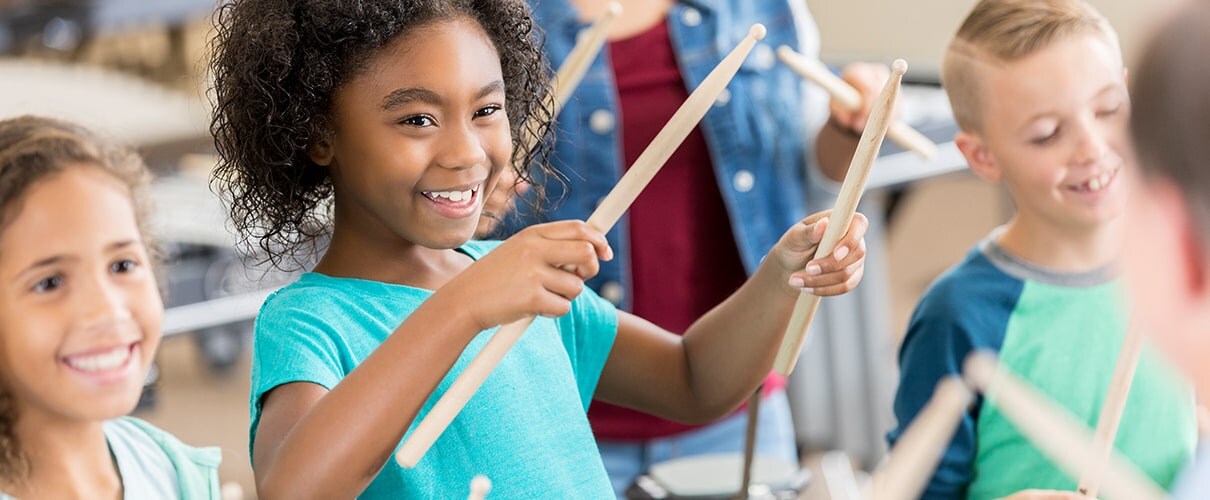 Children in a classroom with drumsticks in their hands playing music