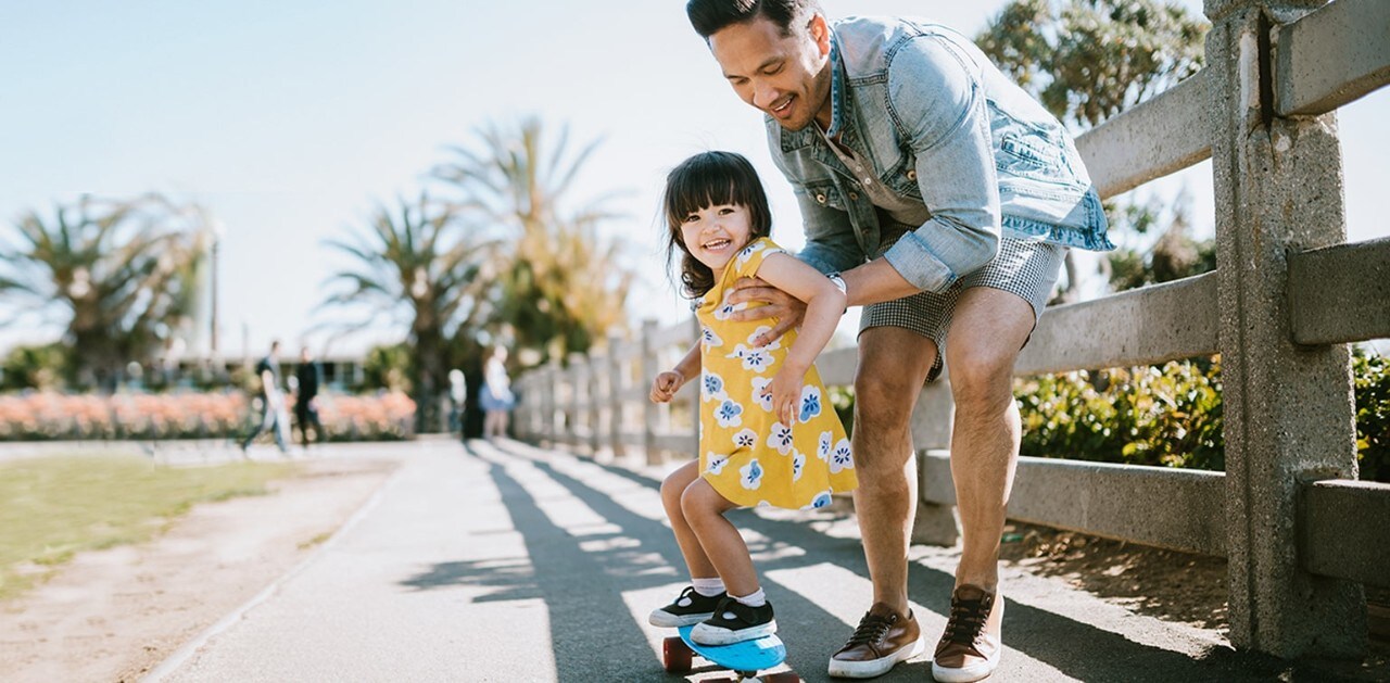 Asian father helping young daughter ride a skateboard