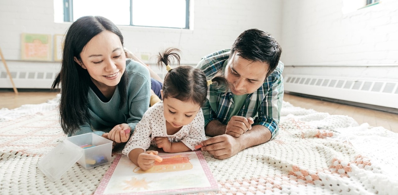 Young Asian girls using a coloring book on the floor with her parents
