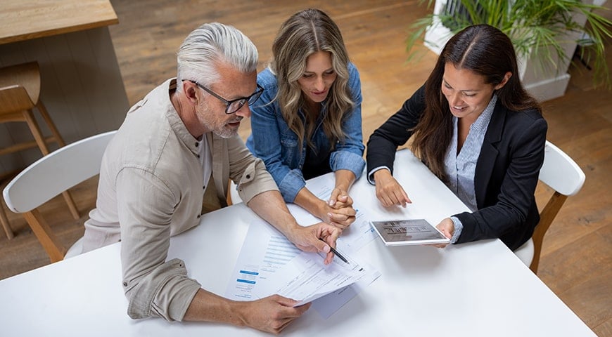 Couple reviewing documents and data on a tablet with their financial advisor