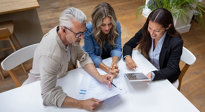 Couple reviewing documents and data on a tablet with their financial advisor